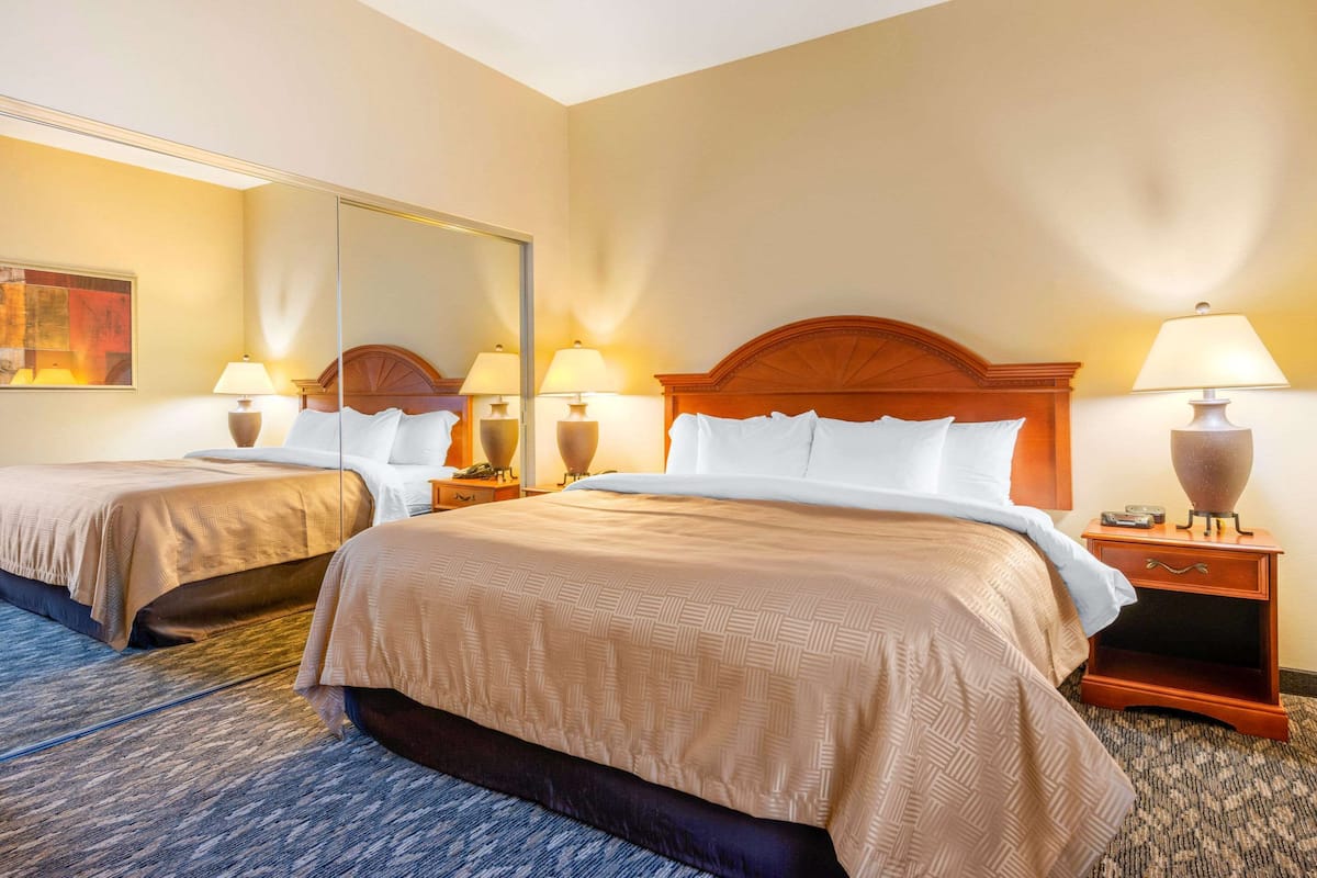 Habitación de hotel con dos camas, un espejo grande, lámparas de noche y suelo alfombrado.