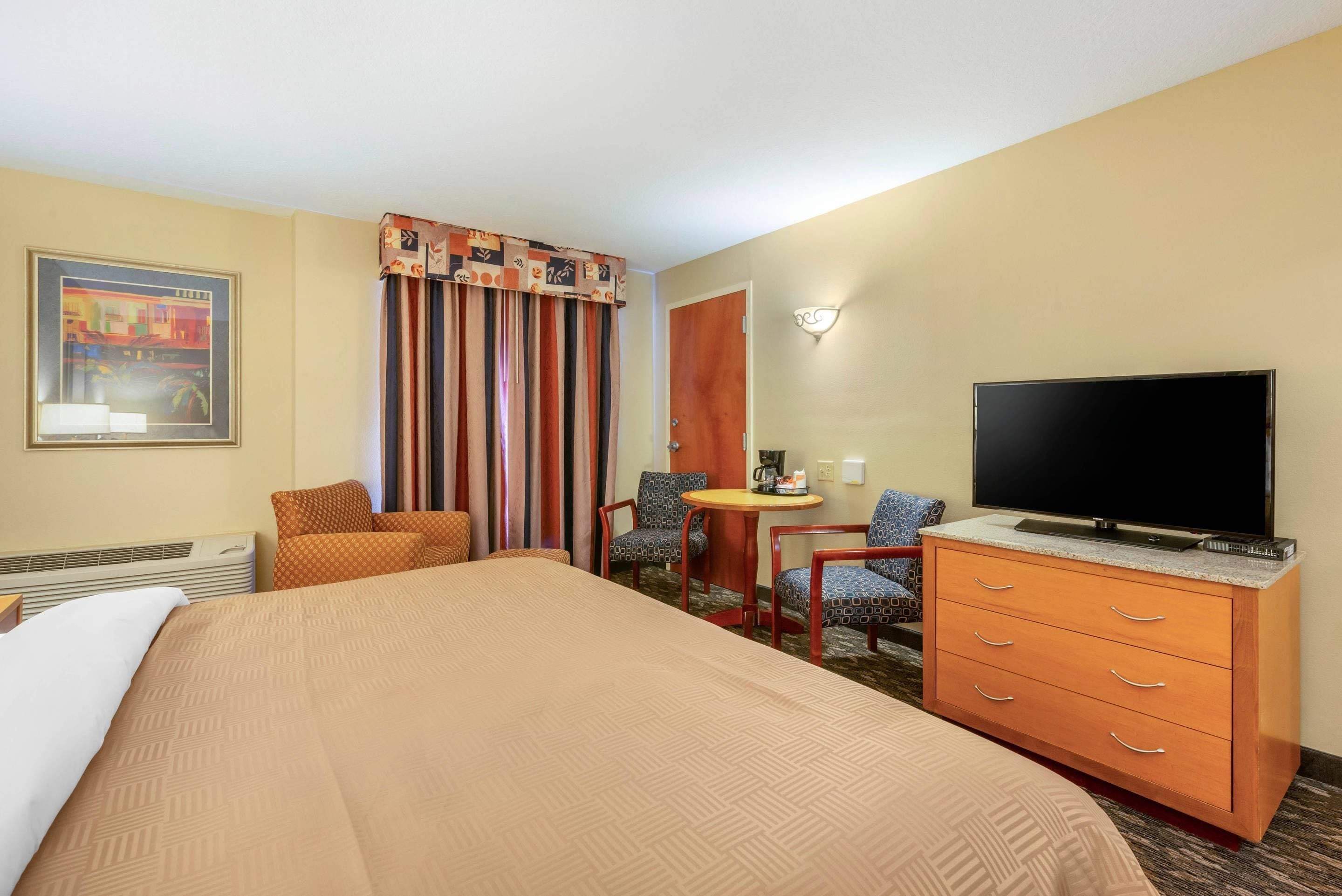 A hotel room with a bed, a desk with a chair, a television, and a wall-mounted light fixture.