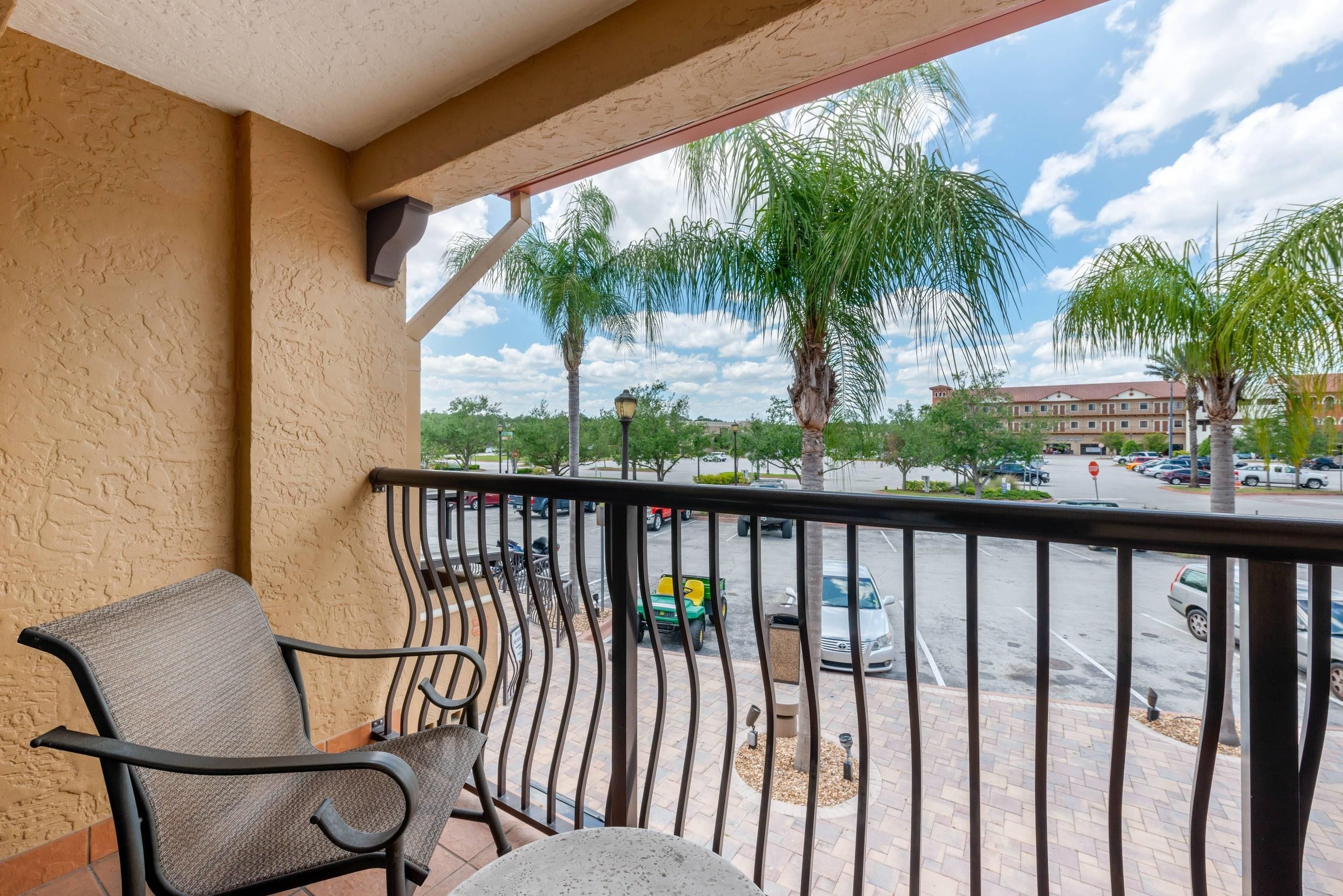 A balcony with a chair, a view of a parking lot, and a building in the background.