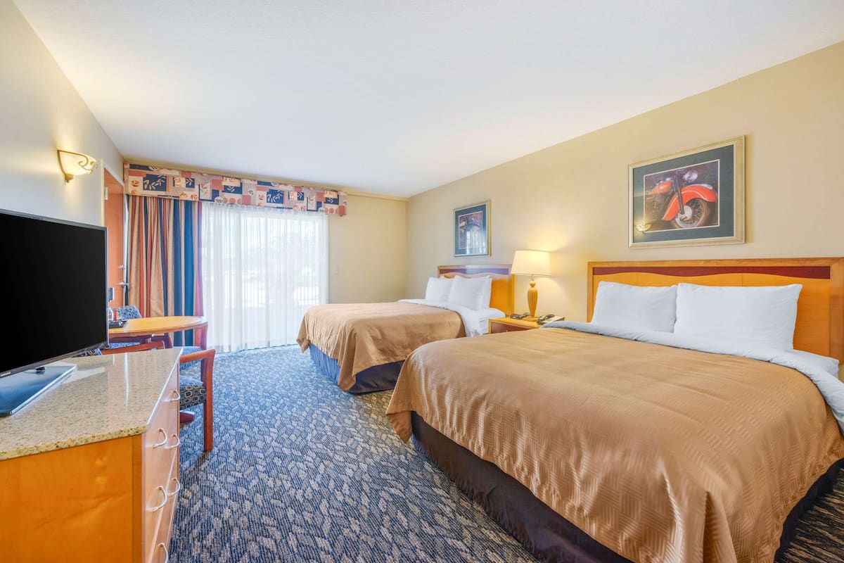 Habitación de hotel con dos camas, un escritorio con televisor y una ventana con cortinas.