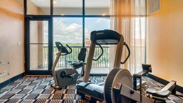 Un gimnasio con máquinas de cardio y una banca, ventanas amplias con vistas, y un suelo con diseño.