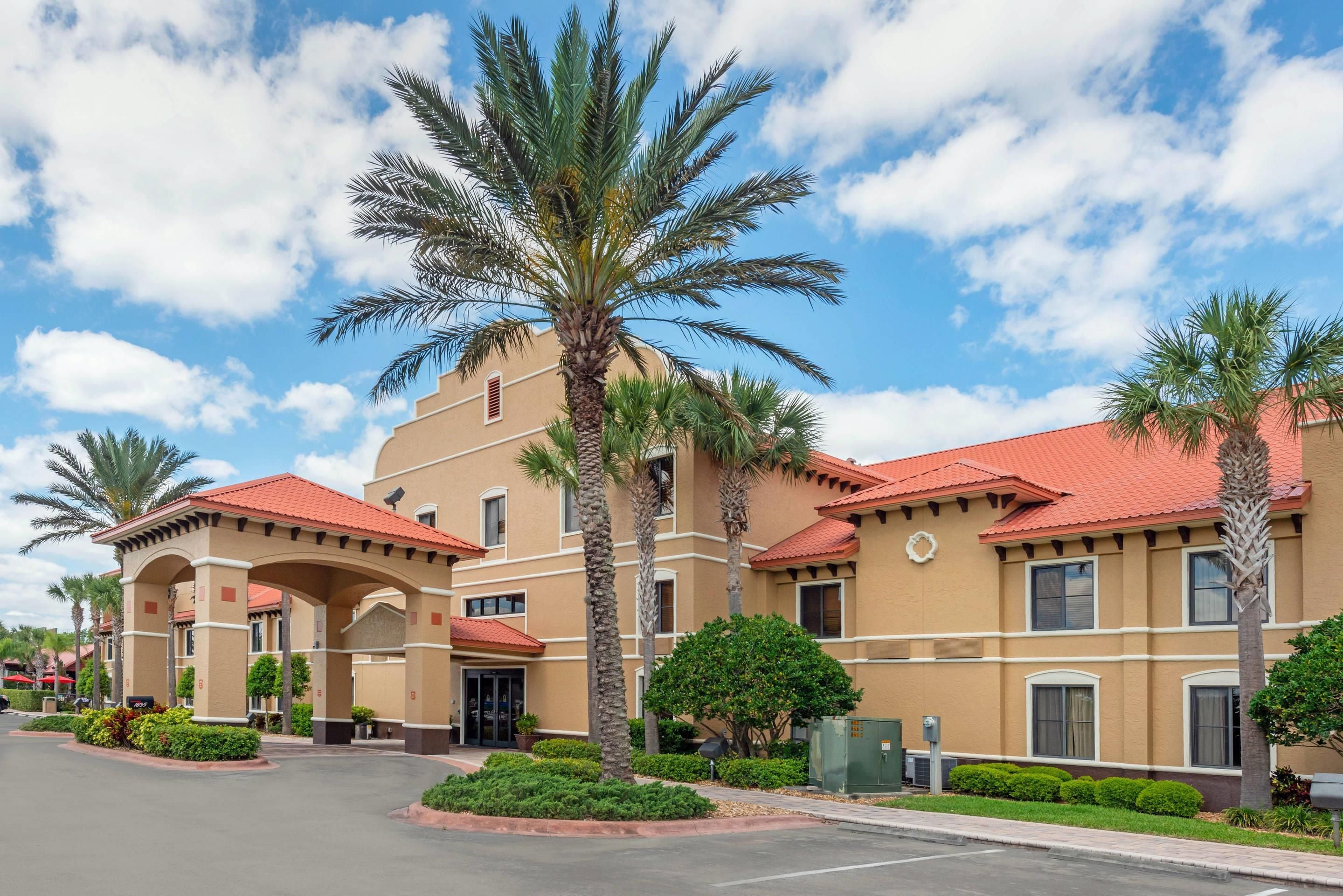 A hotel with a red-tiled roof, palm trees, and a clear sky.