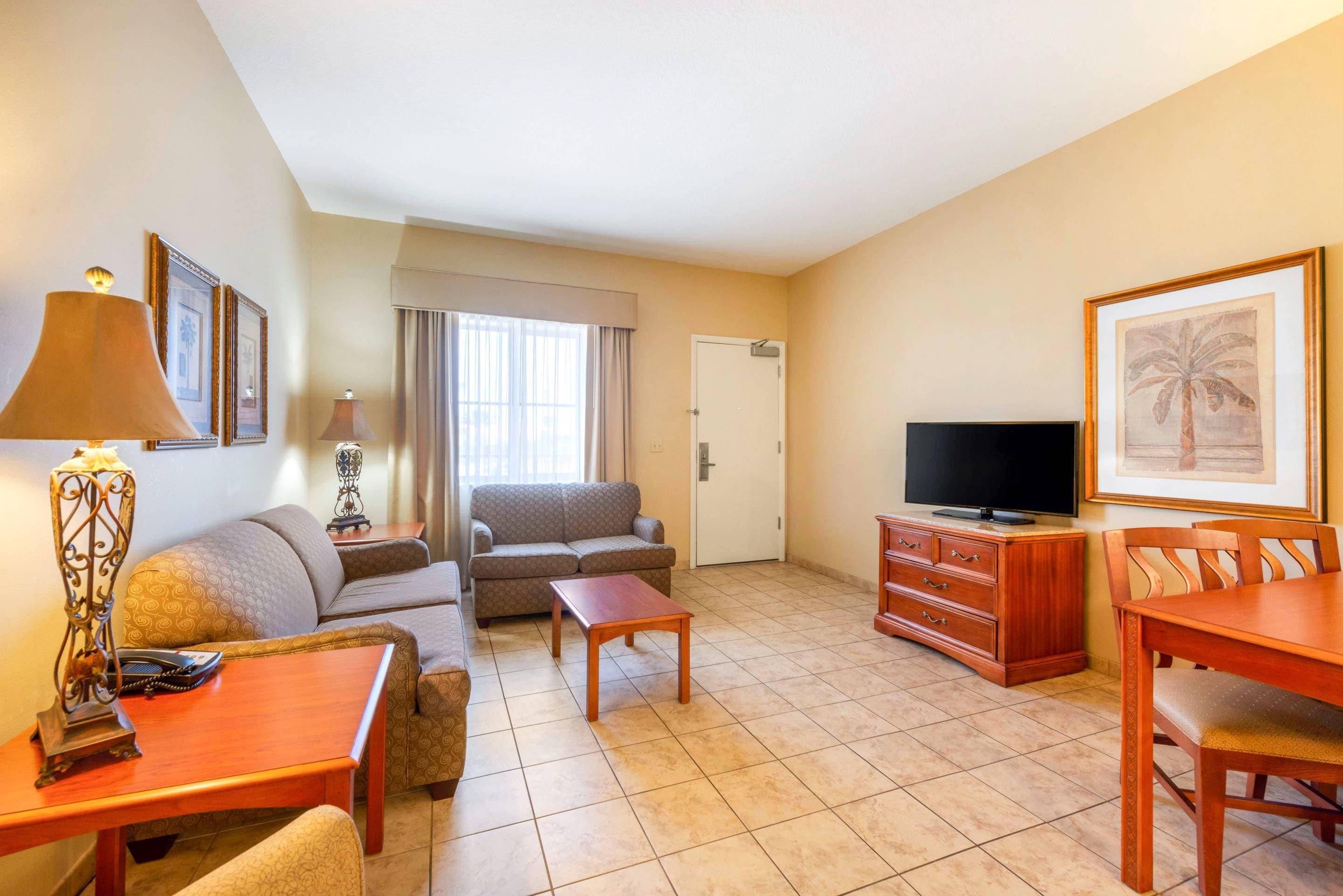 A hotel room with a sofa, a coffee table, a TV, a dining table, and a chair.