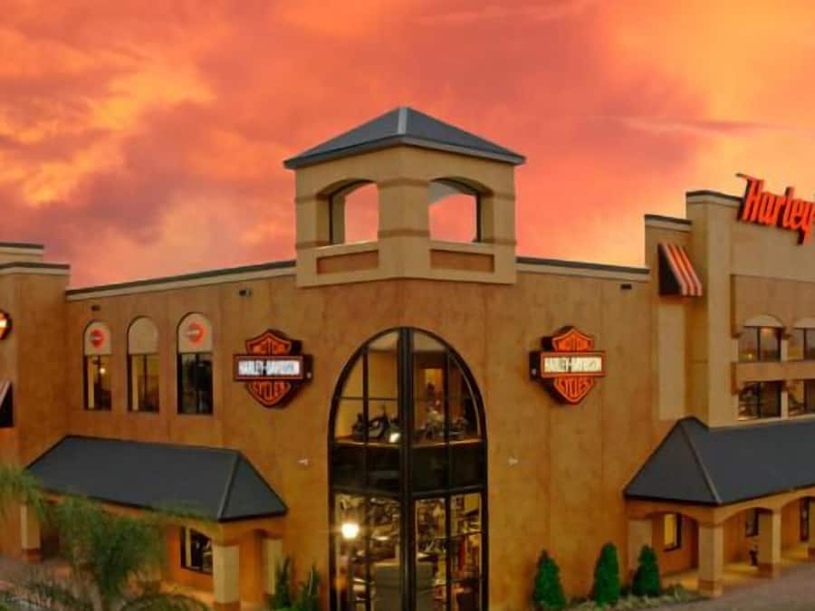 A Harley-Davidson branded building with a large arched entrance, multiple windows, and a parking area in front.