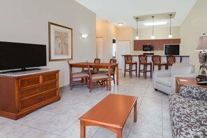 A living room with a TV, wooden furniture, a dining area with chairs, and a kitchen with a microwave. - Clarion Inn Ormond Beach at Destination Daytona (Ormond Beach)