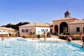 A swimming pool area with people, a building with a tiled roof, and a clock tower.