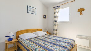 Une chambre à coucher avec un lit en bois, une table de chevet avec une lampe, une fenêtre avec un rideau et un radiateur fixé au mur.