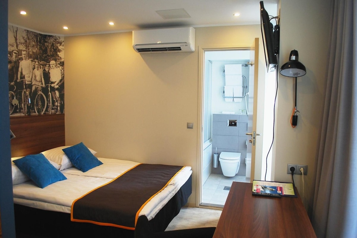 A hotel room with a bed, a desk, a TV, and a bathroom visible through an open door.