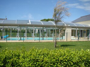 A covered swimming pool with a transparent roof, surrounded by a fenced area and lush greenery. - Résidence Lagrange Vacances le Hameau de Peemor Pen (Crozon)