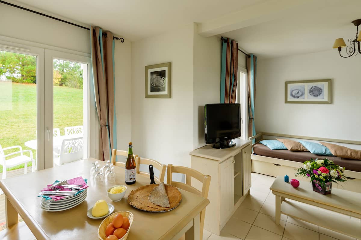 A cozy living room with a sofa, a TV, and a dining area with a table set for a meal.