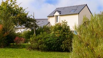 A house with a sloped roof, surrounded by lush greenery and a well-maintained lawn.