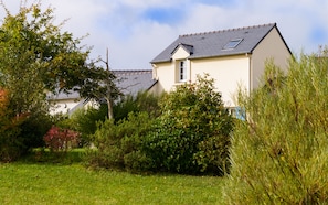A house with a sloped roof, surrounded by lush greenery and a well-maintained lawn.