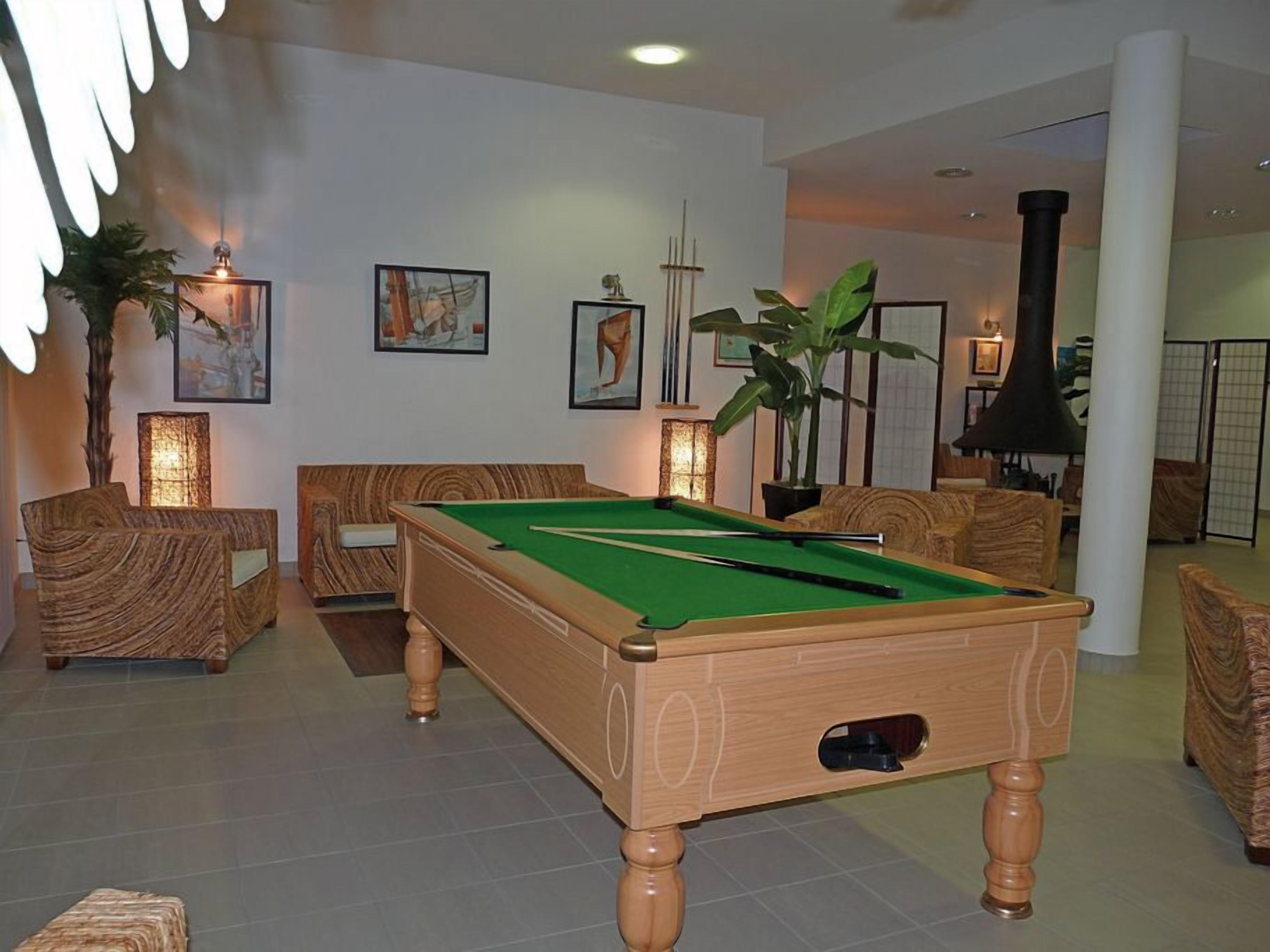 A pool table in a room with wooden furniture, framed artwork on the walls, and a large plant.