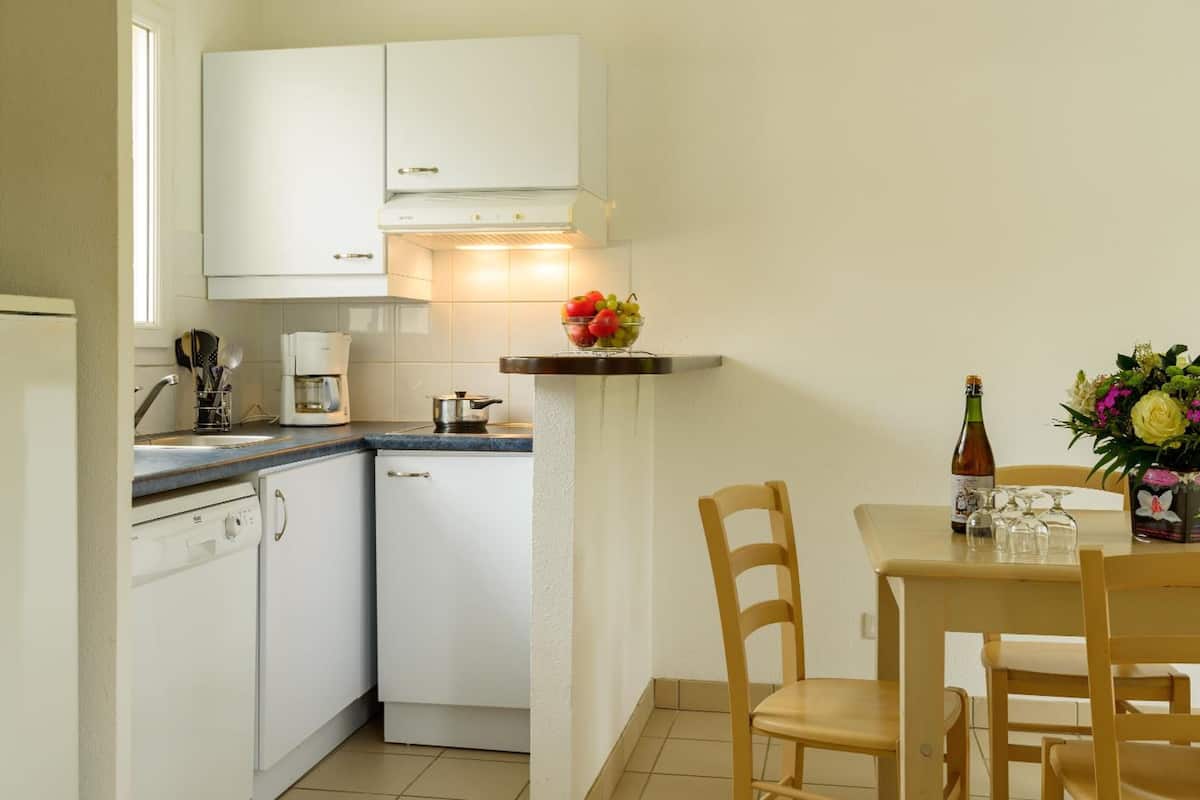A compact kitchen with white cabinets, a coffee maker, and a small dining area with two chairs and a table.