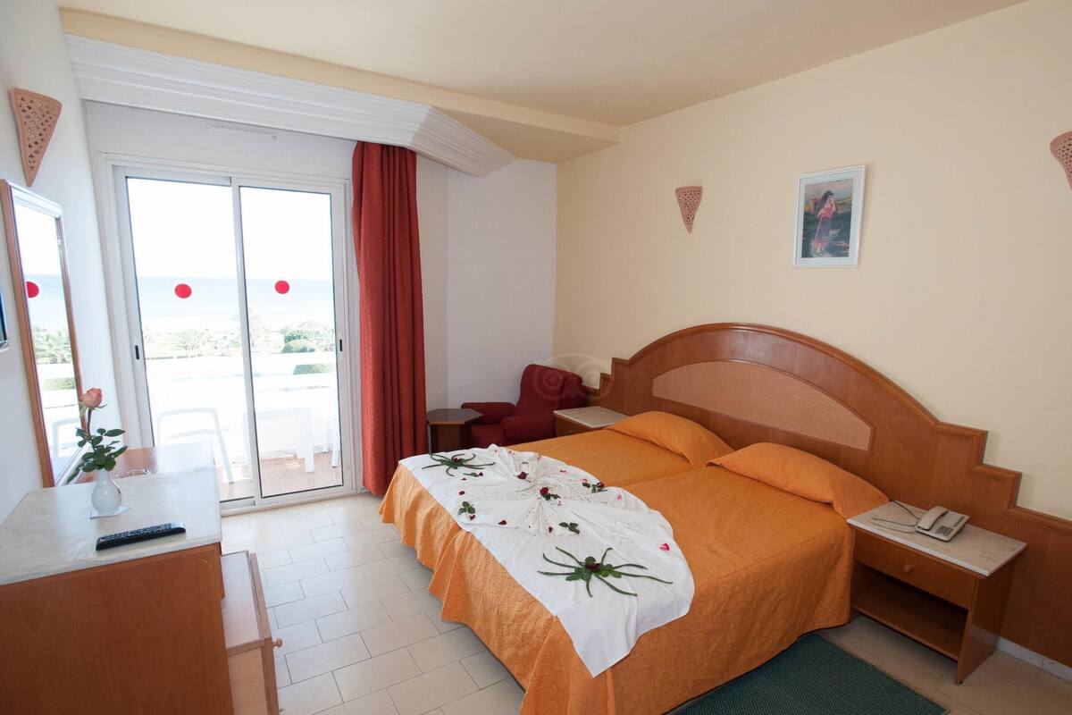 Une chambre d’hôtel avec un lit, un bureau, une chaise, une table de chevet et une fenêtre avec des rideaux.