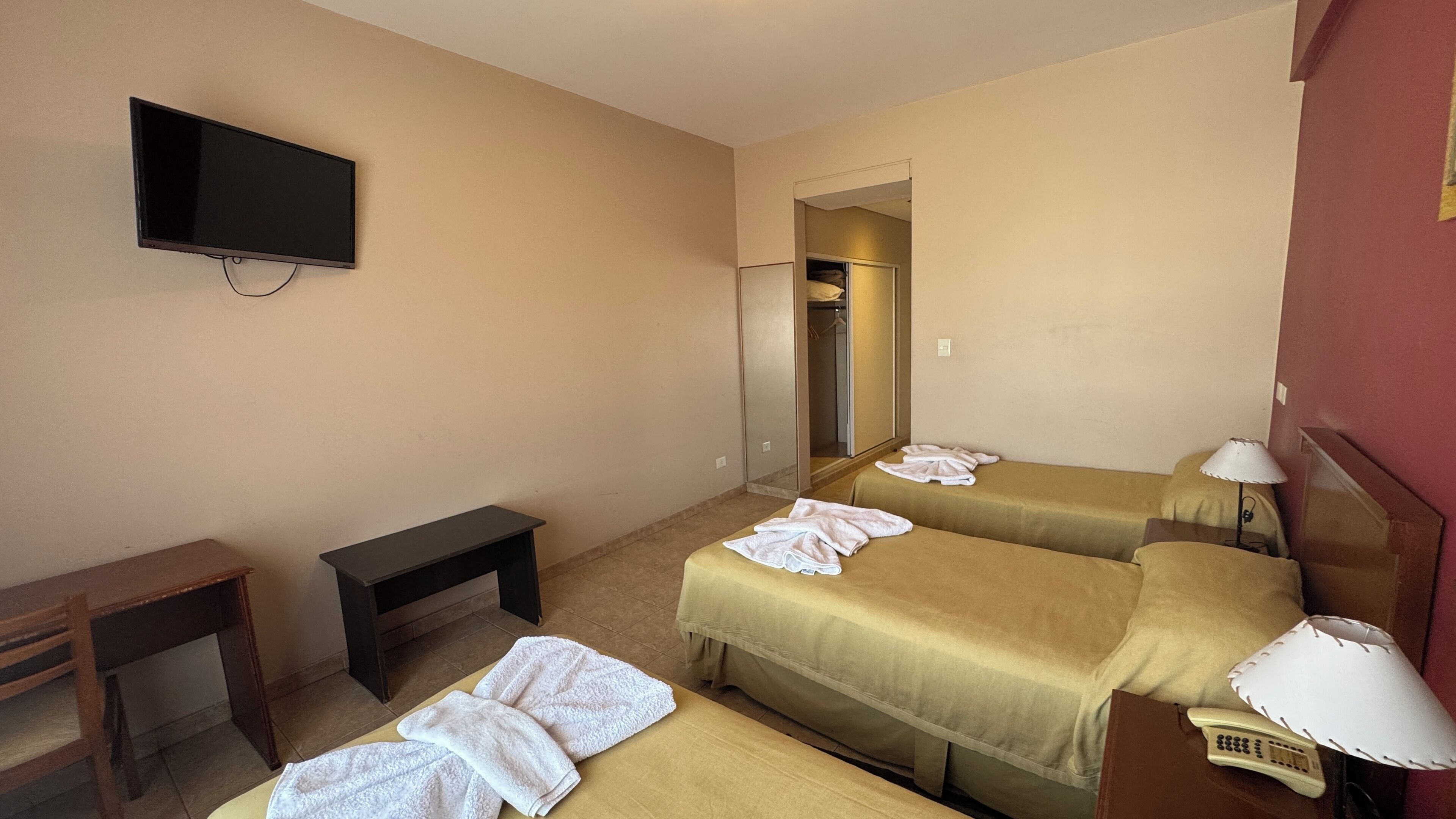 A hotel room with two beds, a TV, a desk, a mirror, and a bathroom visible through an open door.