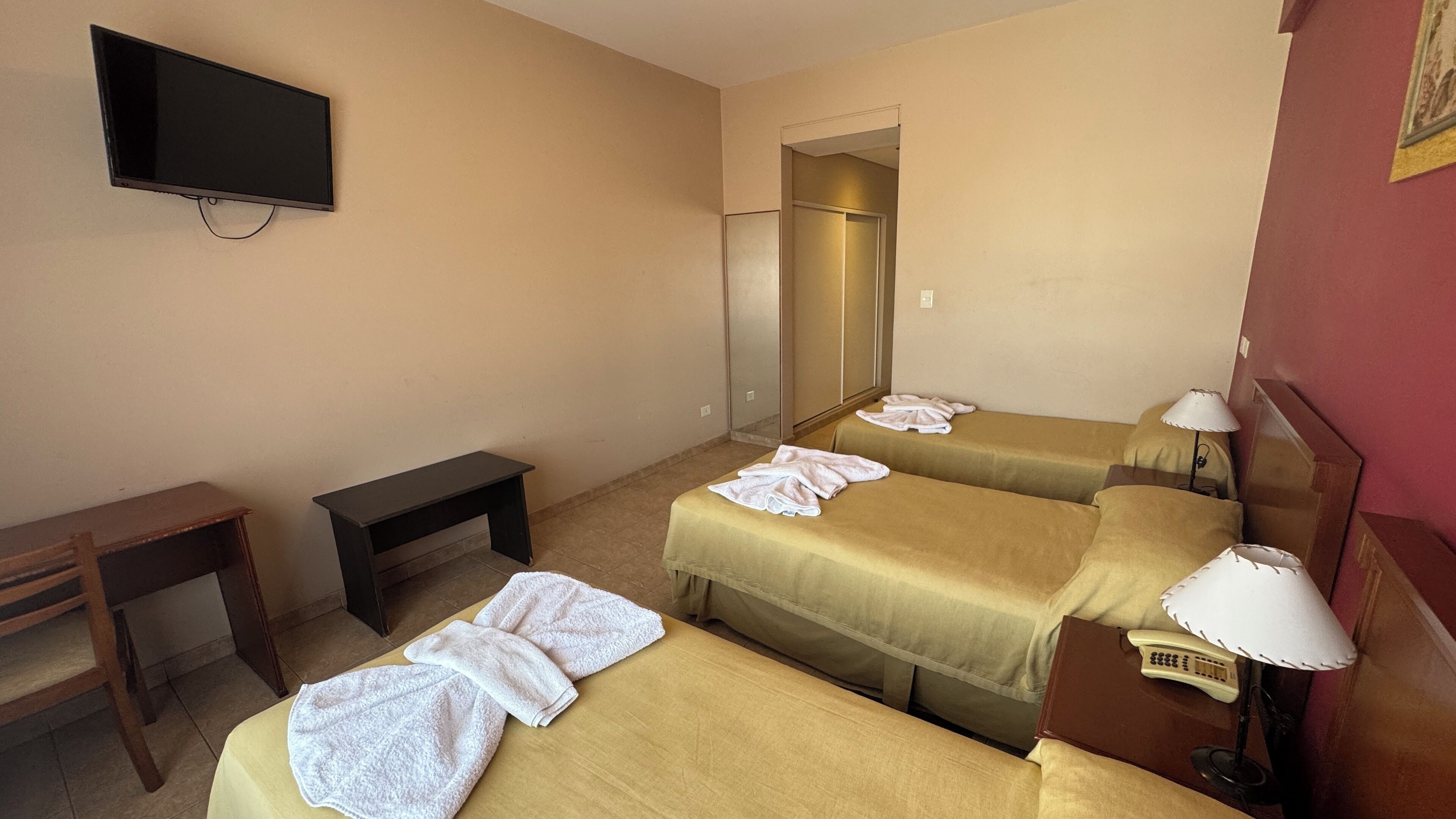 A hotel room with two beds, a desk, a TV, and a mirror.