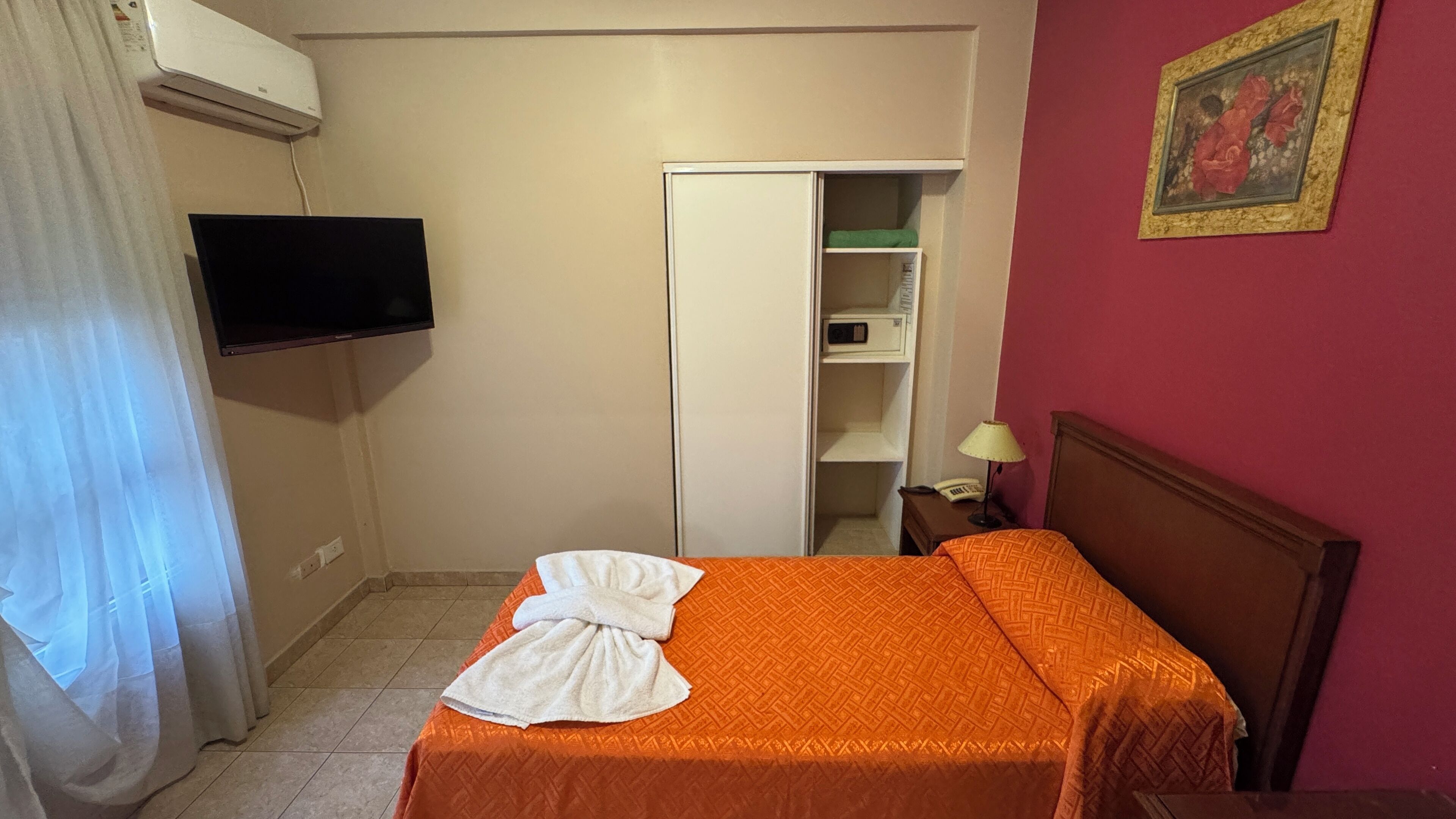A hotel room with a bed, a TV mounted on the wall, a wardrobe, and a bedside table with a lamp.