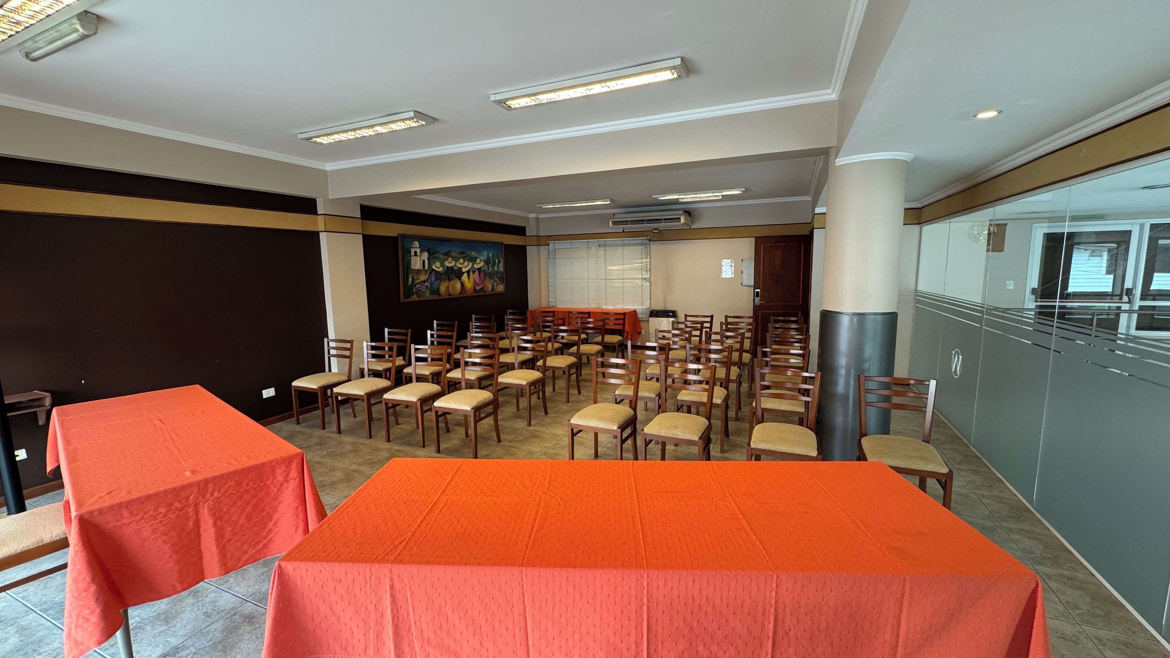 A conference room with tables and chairs, a painting on the wall, and an air conditioning unit.