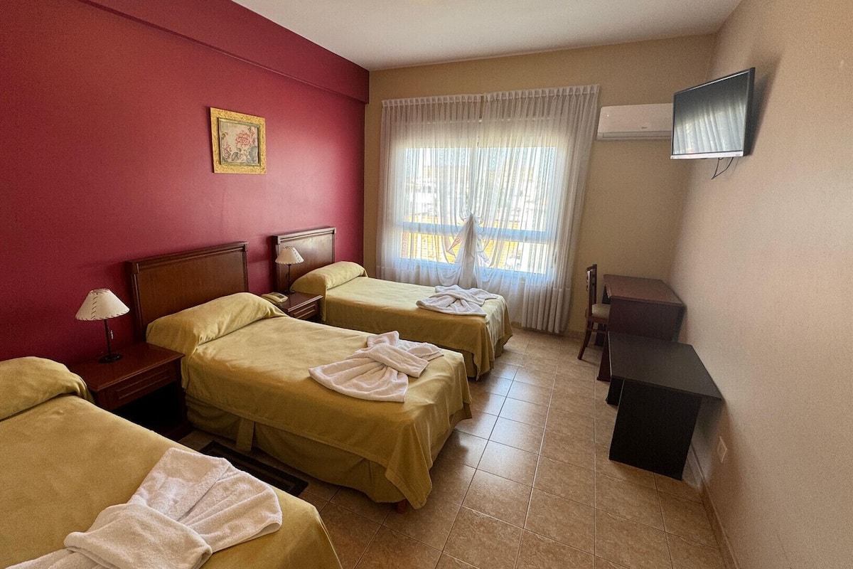 A hotel room with two beds, a desk, a chair, a TV, and a window with curtains.