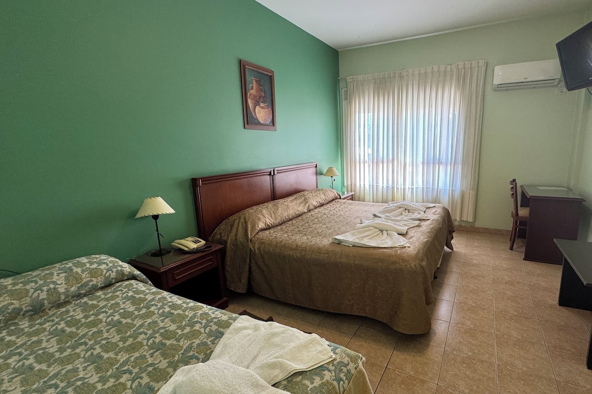 A hotel room with a bed, a desk, a chair, a lamp, a telephone, and a painting on the wall.