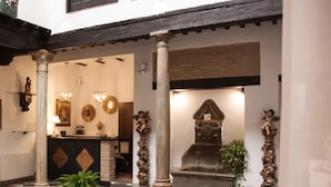 A lobby with a reception desk, columns, a fountain, and decorative elements. - Hotel Rosa D´Oro (Granada)