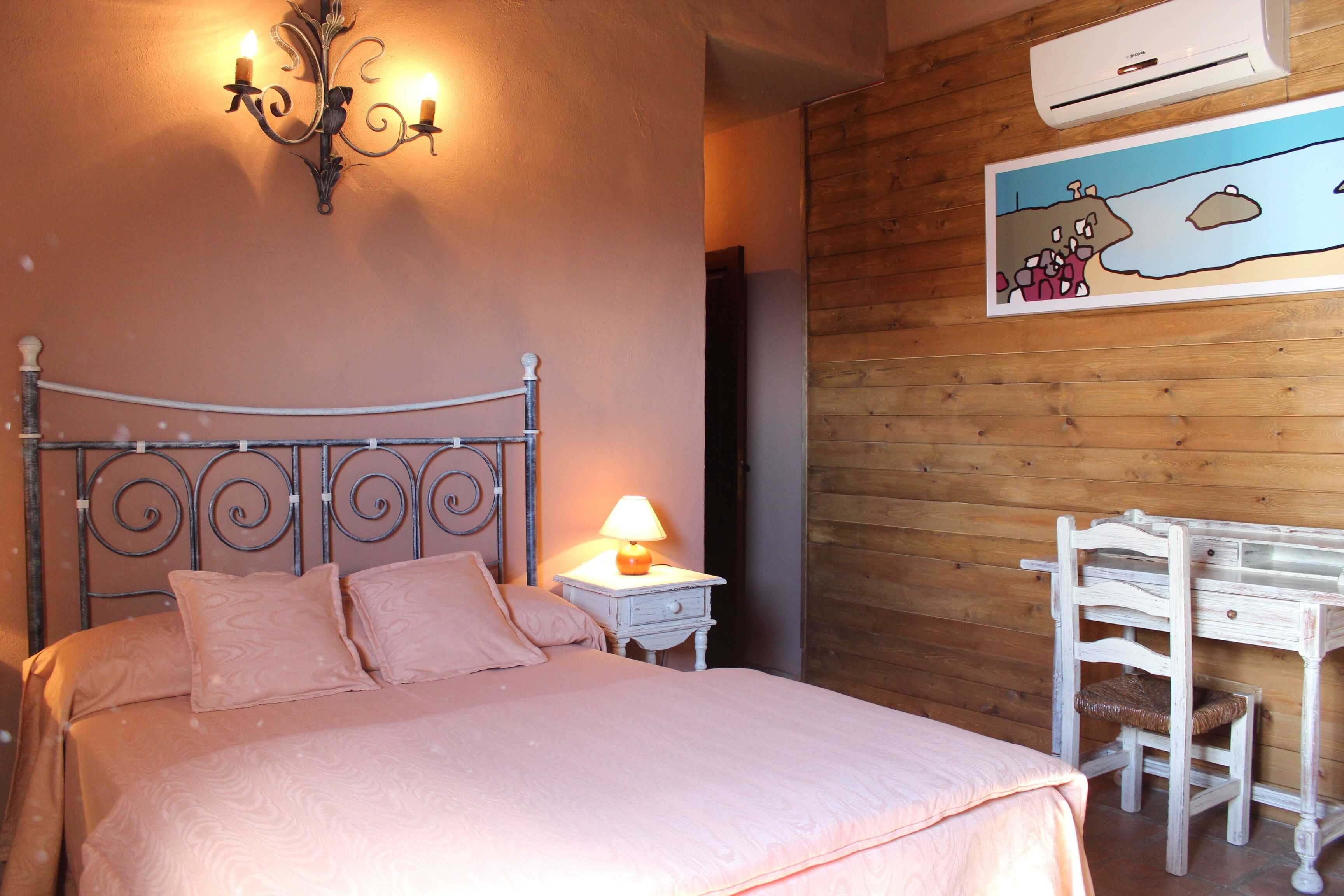 A bedroom with a bed, bedside table, lamp, and a wall-mounted air conditioner.