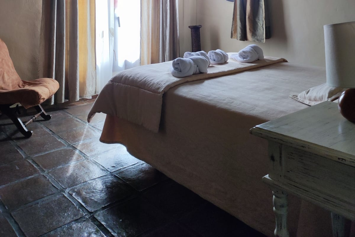 A hotel room with a bed, a chair, a round window, and curtains.