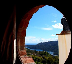 A view through a circular window with a rusty arch, overlooking a landscape with mountains and a body of water. - Hotel Los Jarales (Istan)