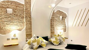 A modern bedroom with a brick wall, a bed with multiple pillows, and a small bedside table. - Complejo Turístico Rural La Garganta (Álora)