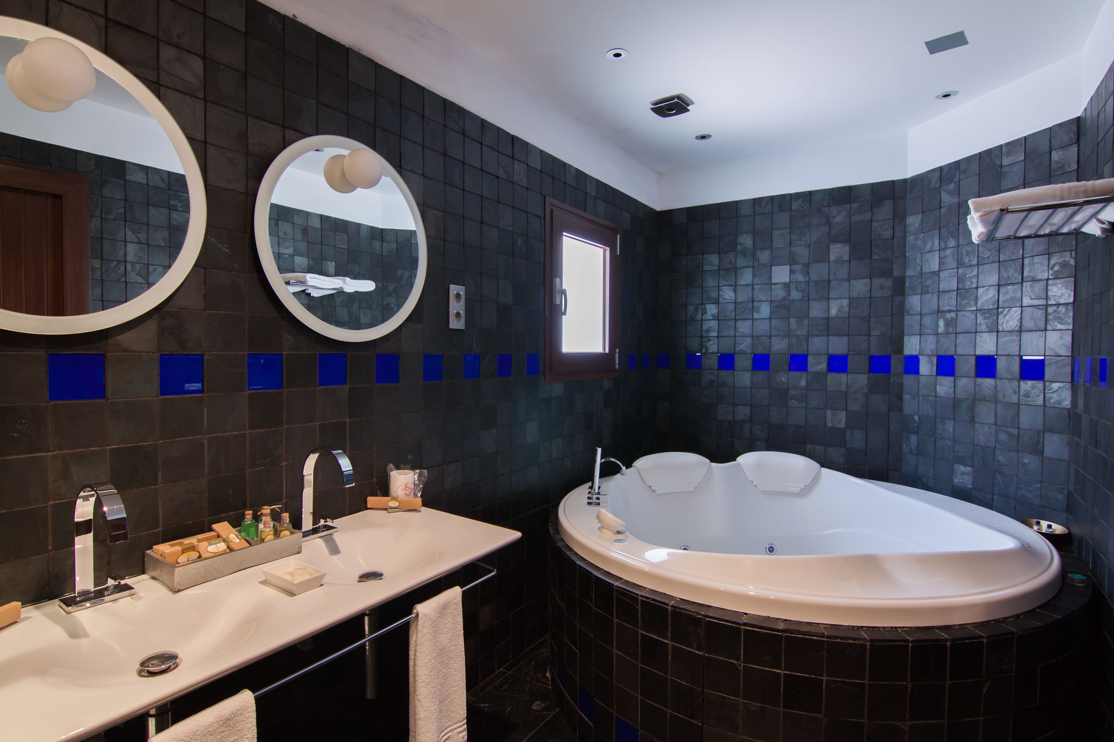 Un baño moderno con una bañera grande, dos lavamanos y dos espejos redondos.