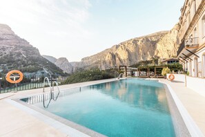 A swimming pool with clear blue water, surrounded by mountains and a building with a balcony.
