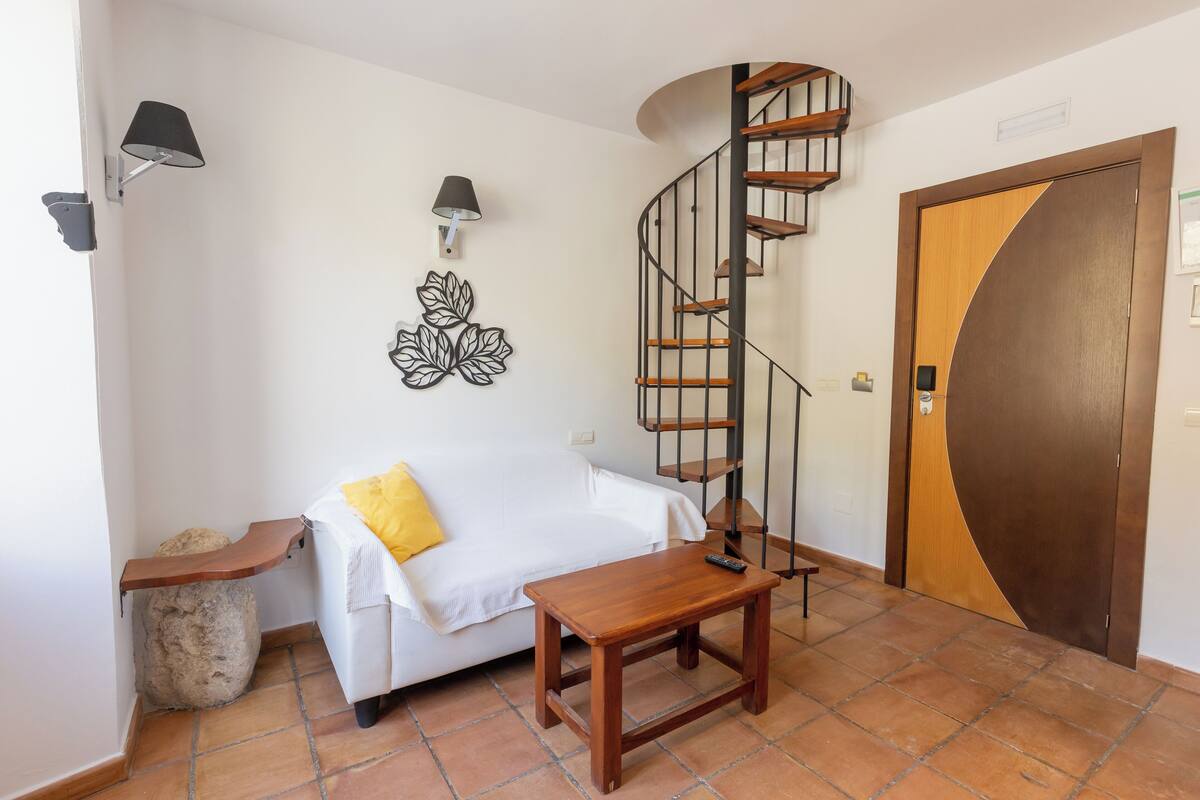 A room with a white sofa, a wooden table, a spiral staircase, and a wooden door.