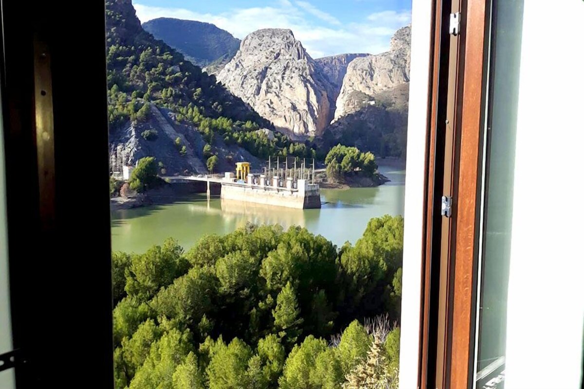 Vista desde el interior de un edificio hacia una represa y la vegetación circundante.