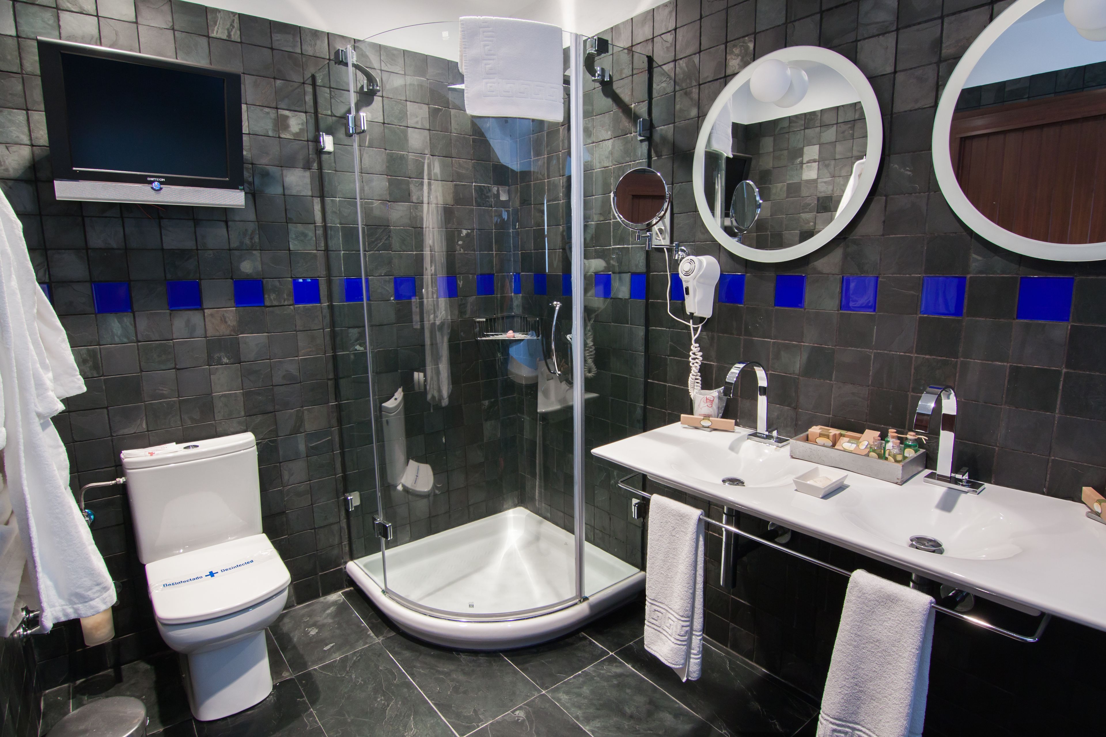 Ein modernes Badezimmer mit einer Duschkabine, Toilette, Waschbecken und einem an der Wand montierten Fernseher.