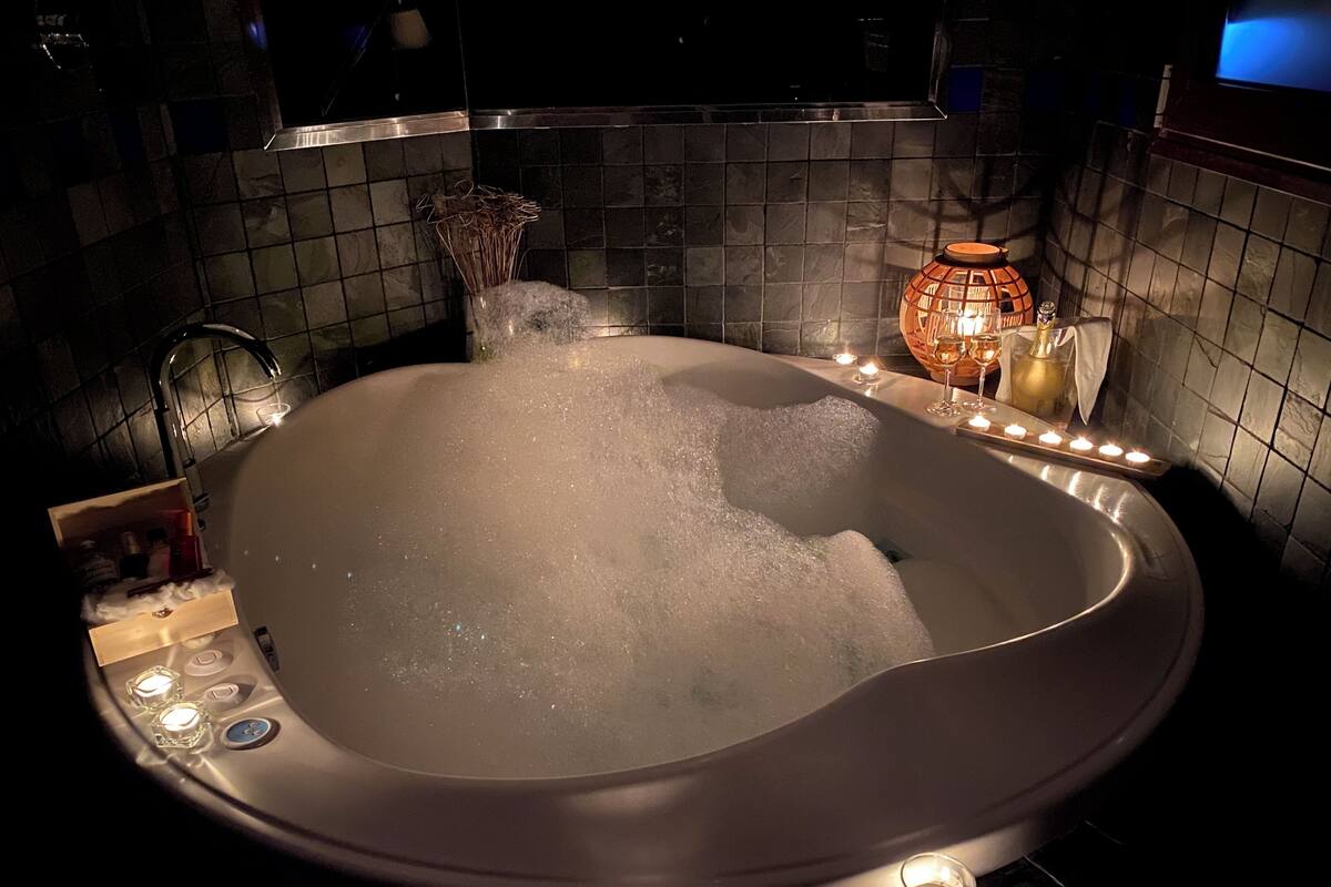 A dimly lit, modern bathroom with a large, oval-shaped bathtub, a glass shower enclosure, and a decorative candle holder.