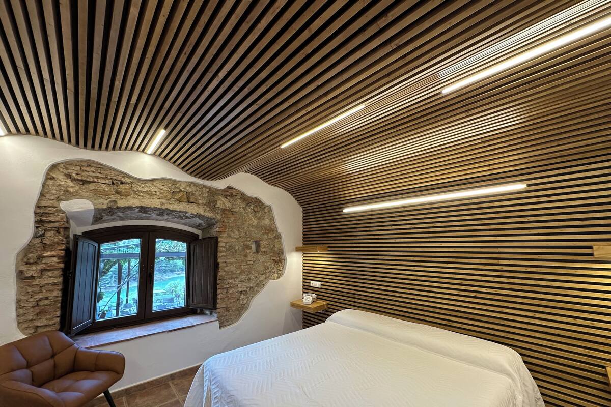 A modern room with a bed, a stone wall, and a window with a view.