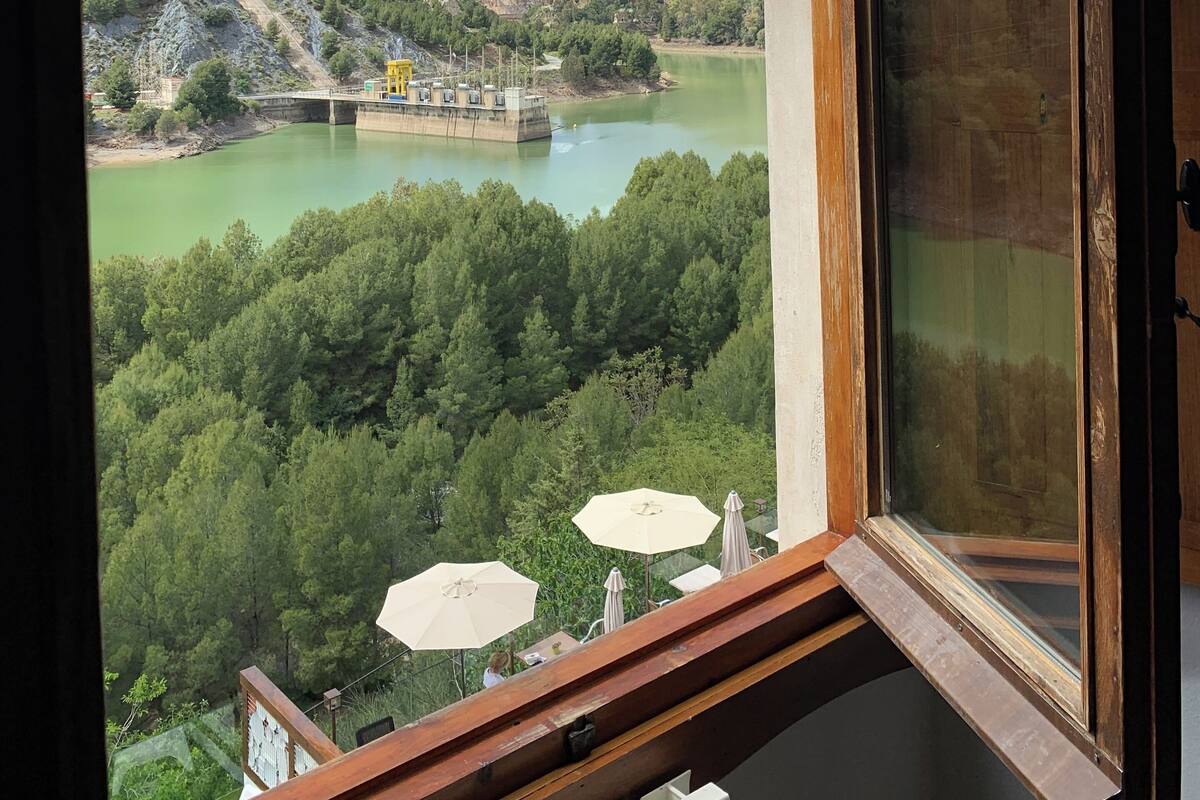 A view from a window overlooking a river, mountains, and a bridge.