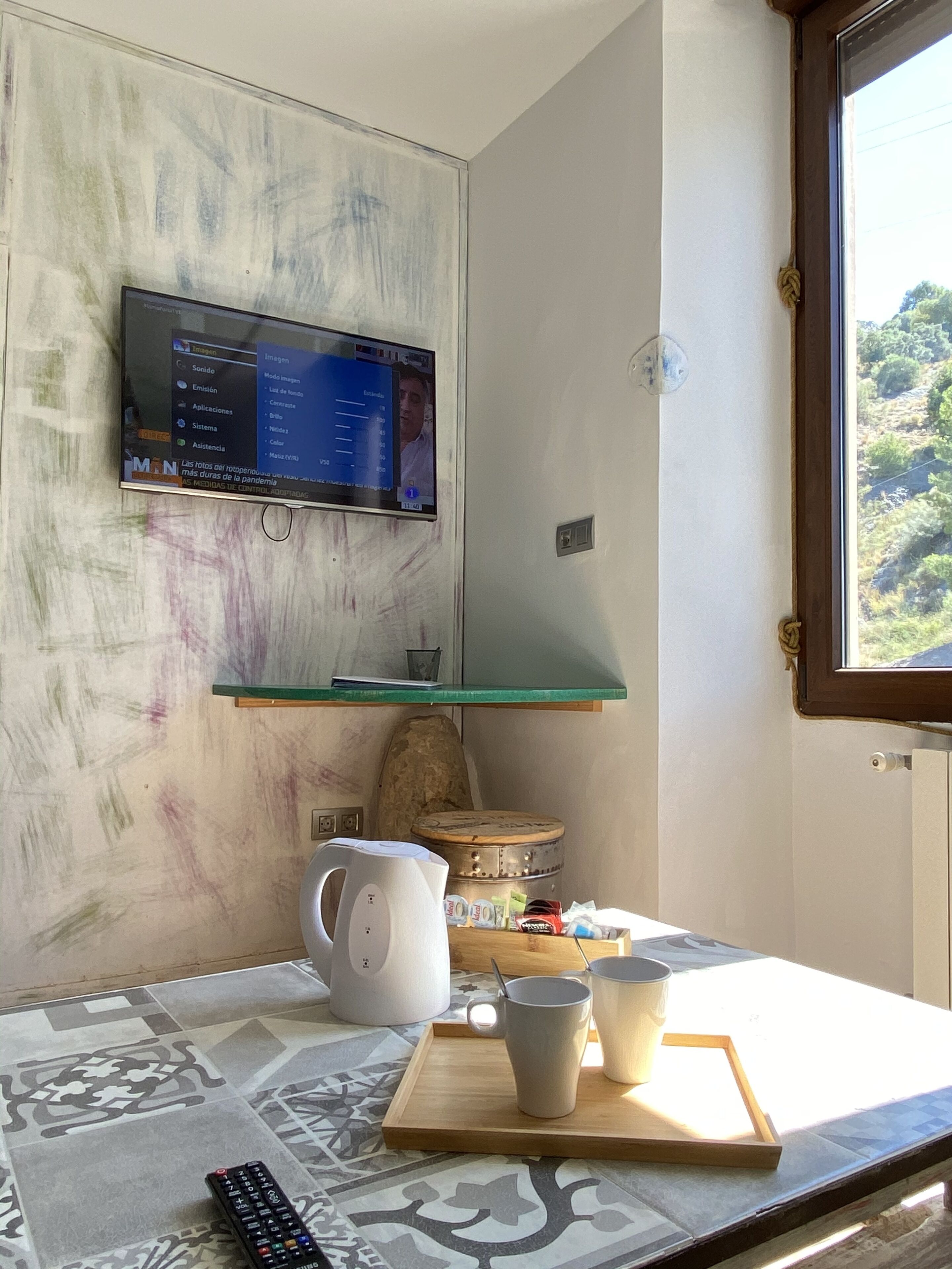 A room with a mounted television displaying a photo gallery, a wooden table with a kettle, cups, and a tray, and a patterned rug.