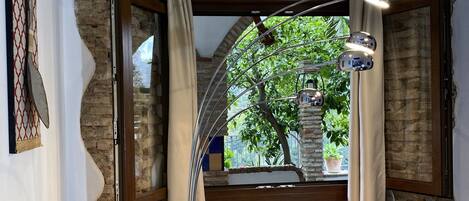 A cozy room with a stone wall, a window with curtains, a reading area with a book and glasses, and a ceiling light.