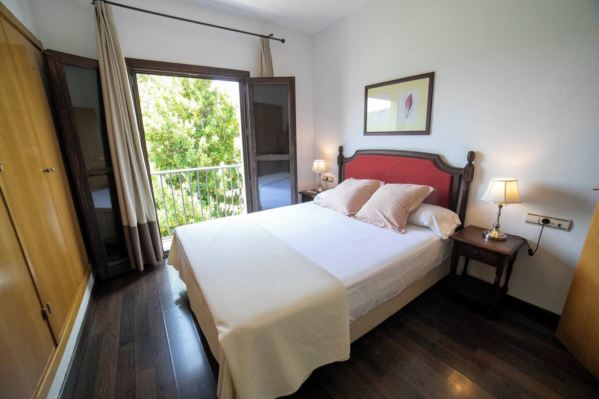 A hotel room with a large bed, two bedside tables with lamps, a wooden wardrobe, and a balcony with curtains.