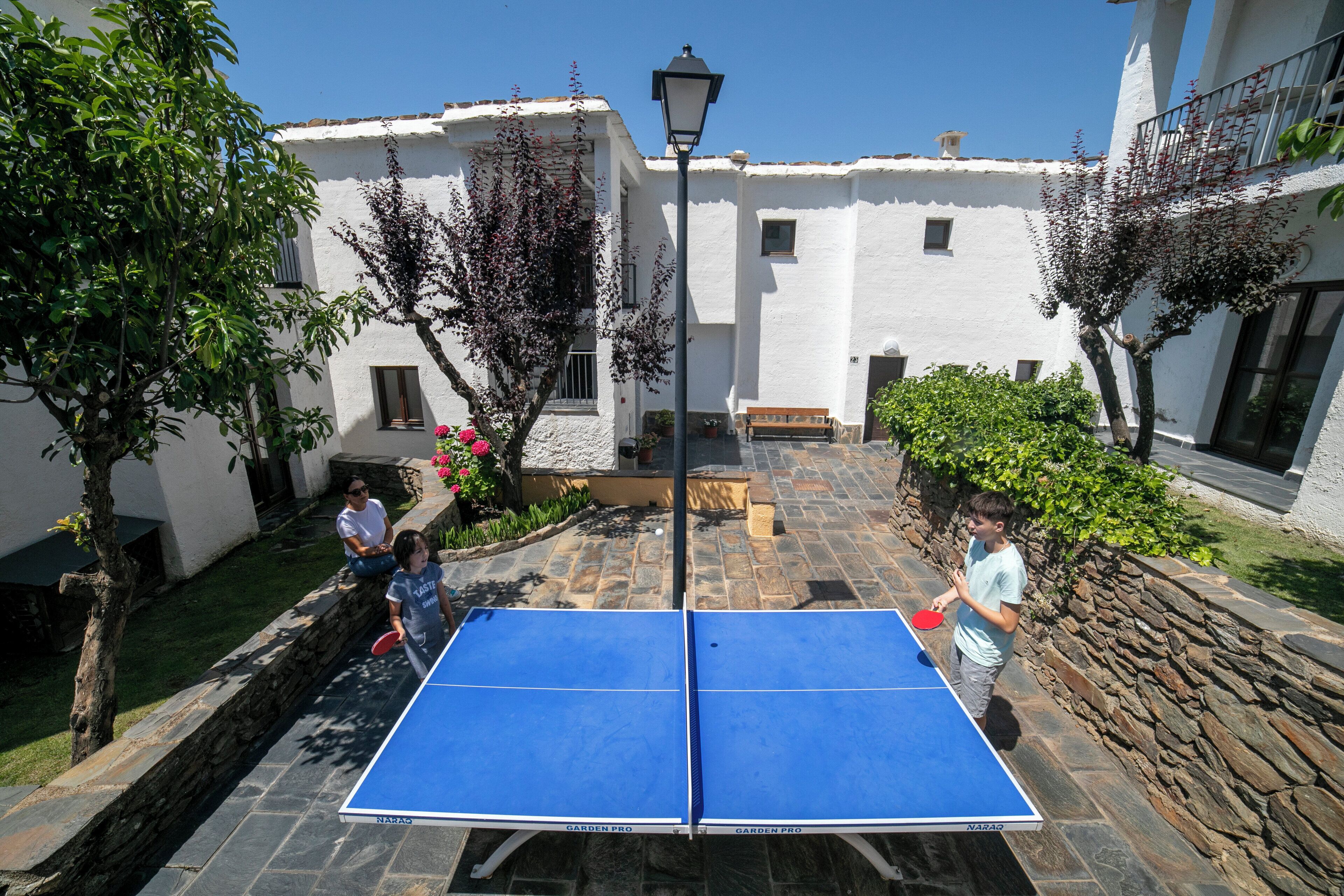 An outdoor ping pong table set up in a courtyard with stone walls and white buildings in the background.