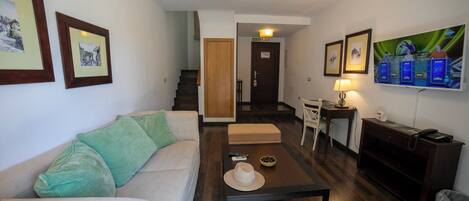 A living room with a sofa, a coffee table, and a TV. There is a staircase leading to another room.