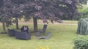 An outdoor seating area with a table and chairs, surrounded by trees and a hedge.