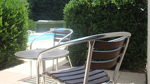A patio area with a pool, metal chairs, and a neatly trimmed hedge. - LOGIS Les Dineux Village (Tremeur)