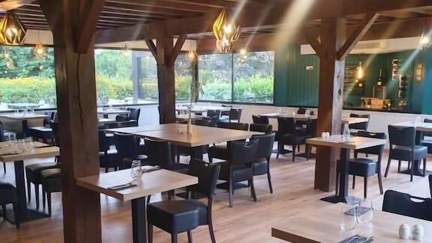 A restaurant with wooden tables and chairs, large windows, and hanging pendant lights. - LOGIS Les Dineux Village (Tremeur)