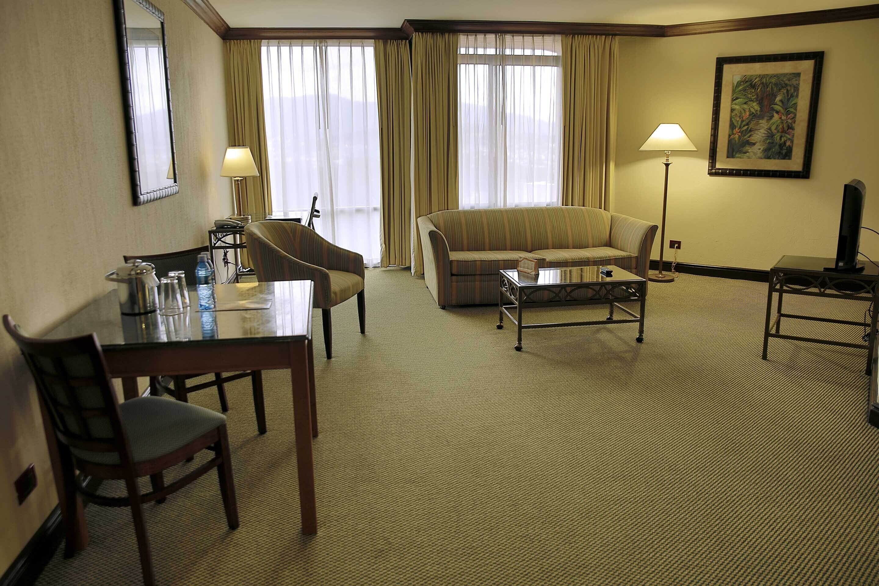 Habitación de hotel con una mesa de comedor, dos sillas, un sofá, una mesa de centro, un televisor y un cuadro en la pared.