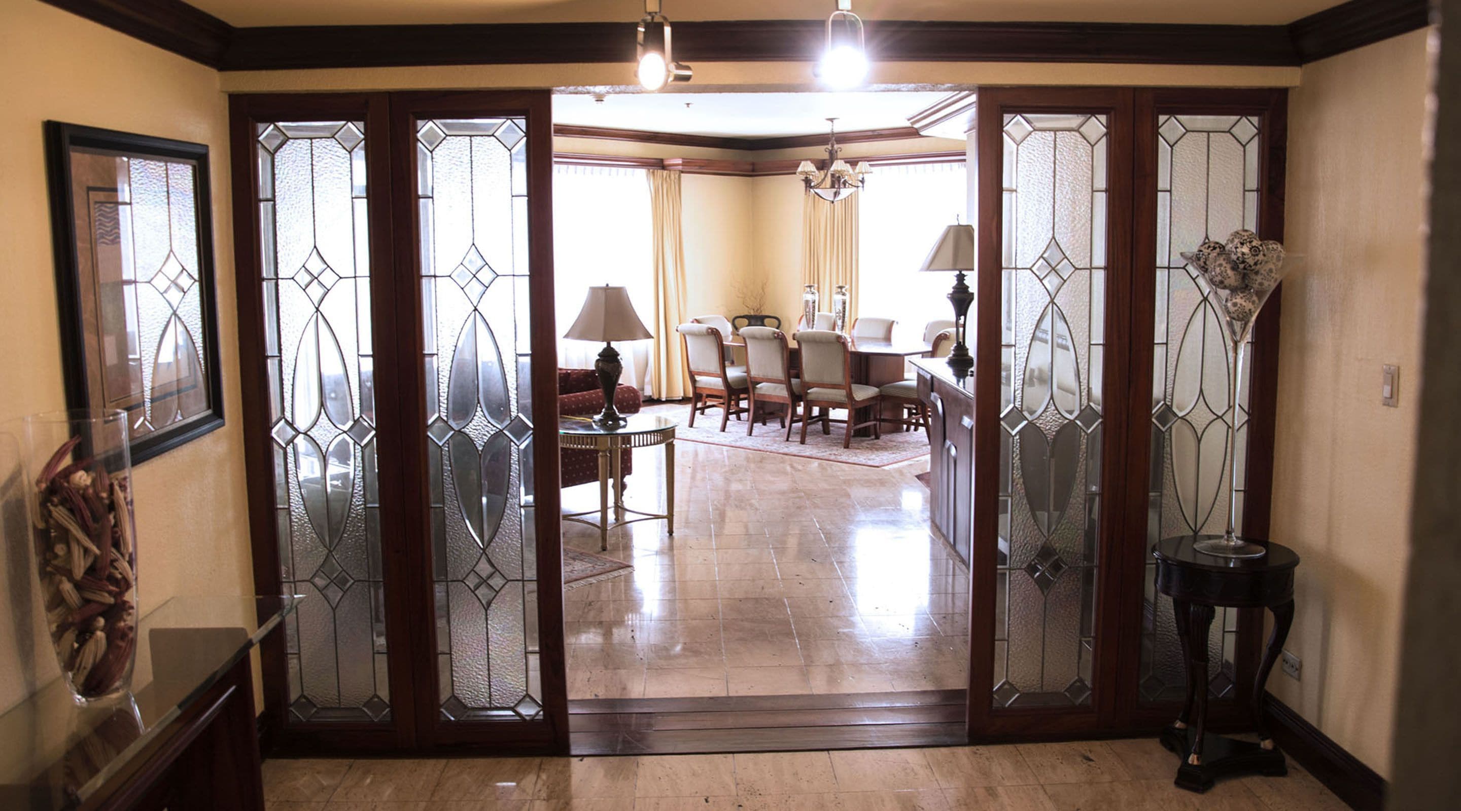 Uma sala de estar ampla com área de jantar, apresentando um grande painel de vidro com desenhos decorativos, um lustre e um vaso com flores secas.