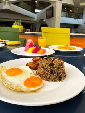 A dining table with plates of food, including fried rice and eggs, in a modern interior with a staircase and hanging plants. - Wyndham San Jose Herradura Hotel & Convention Center (La Asunción)