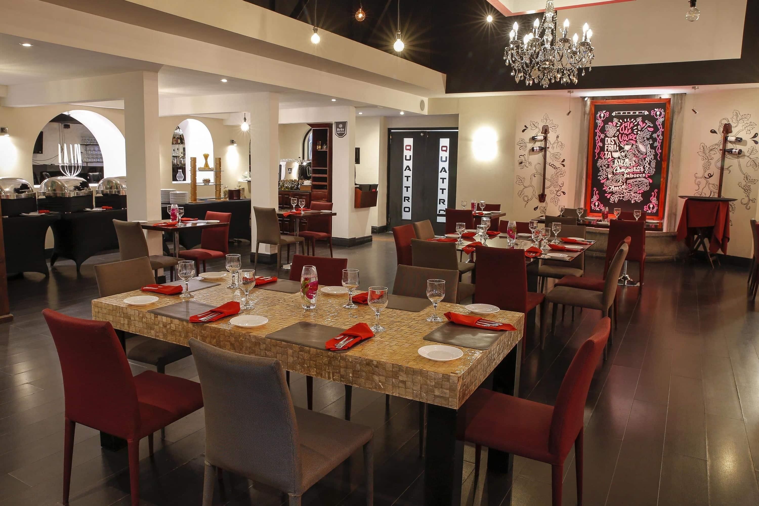 A restaurant with multiple dining tables, red chairs, and a chandelier.